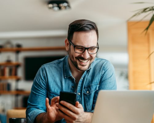 Portrait of a happy man with smart phone and laptop, indoors.